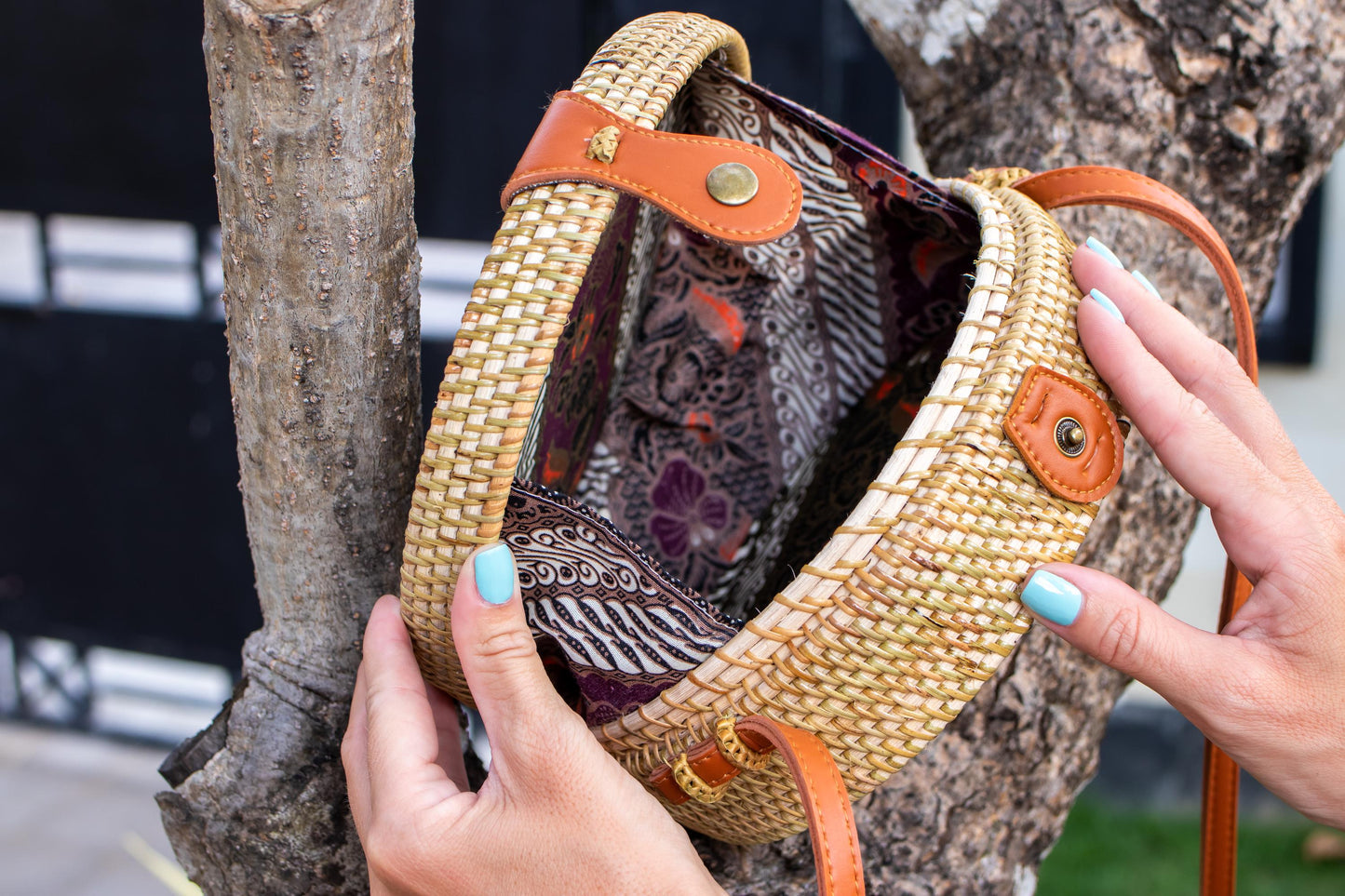 Woven handbag with floral pattern held by a person against a tree.