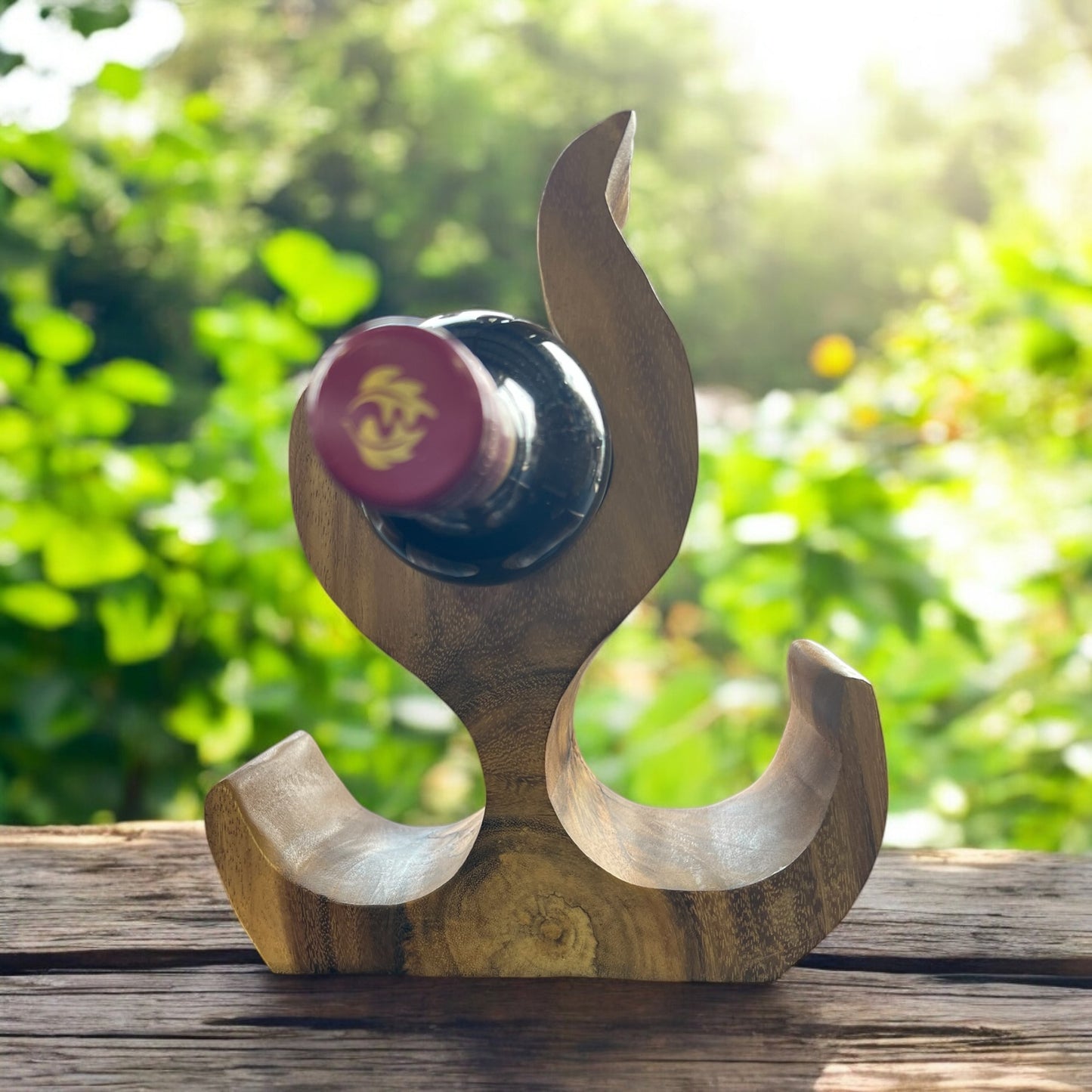 Wooden wine bottle holder with a bottle of red wine against a blurred green outdoor background