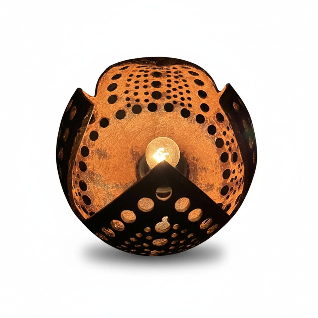 A spherical metal wall sconce with a warm coppery-orange oxidized finish and black cutout patterns, illuminated from within by a central bulb, shown on a white background.