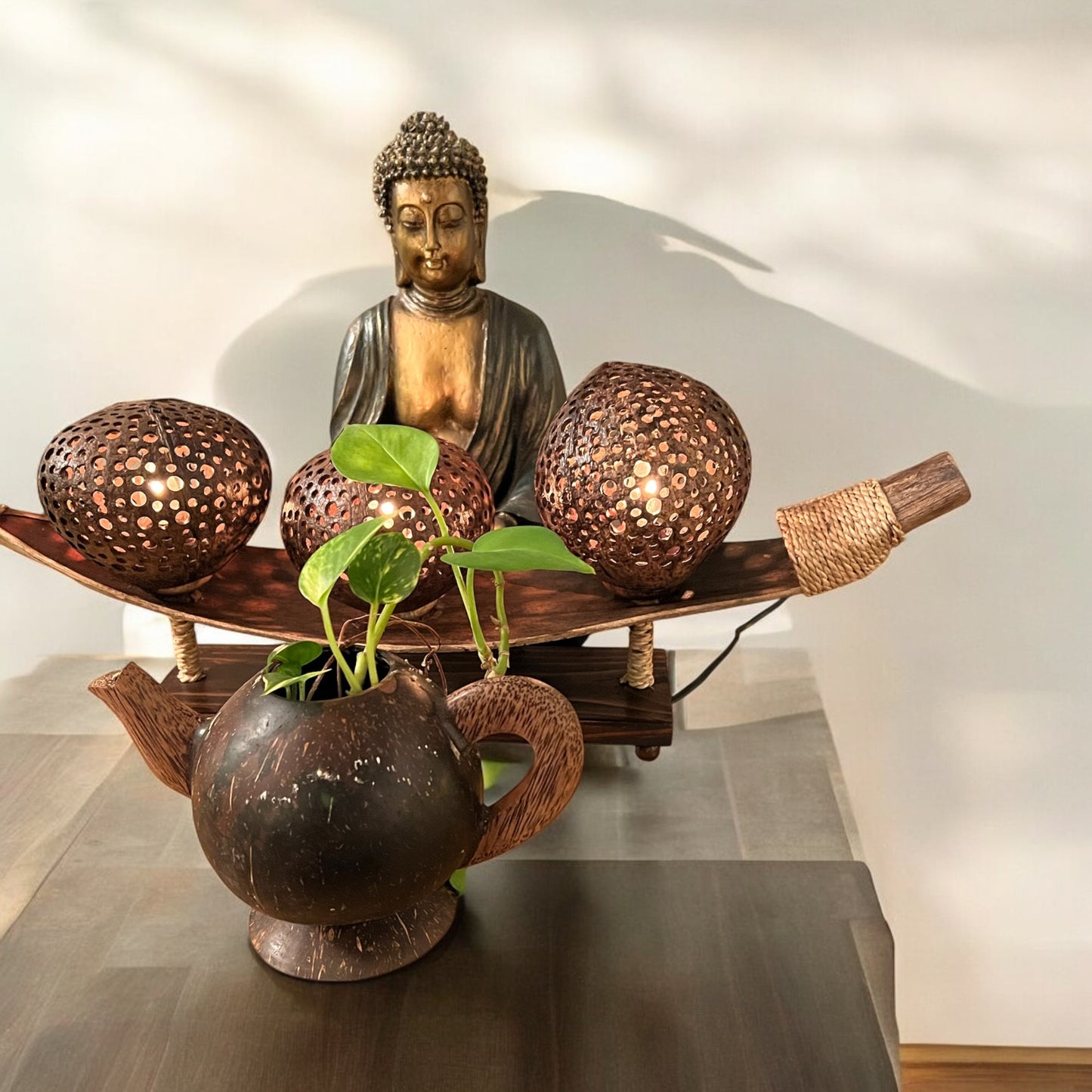 Decorative coconut shell table lamp with a Buddha statue, lanterns, and a teapot on a table.