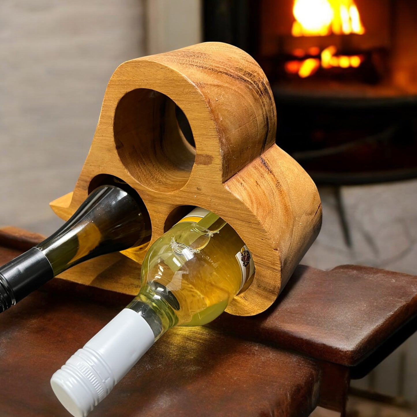 Wooden wine bottle holder with two bottles on a wooden surface, fireplace in the background