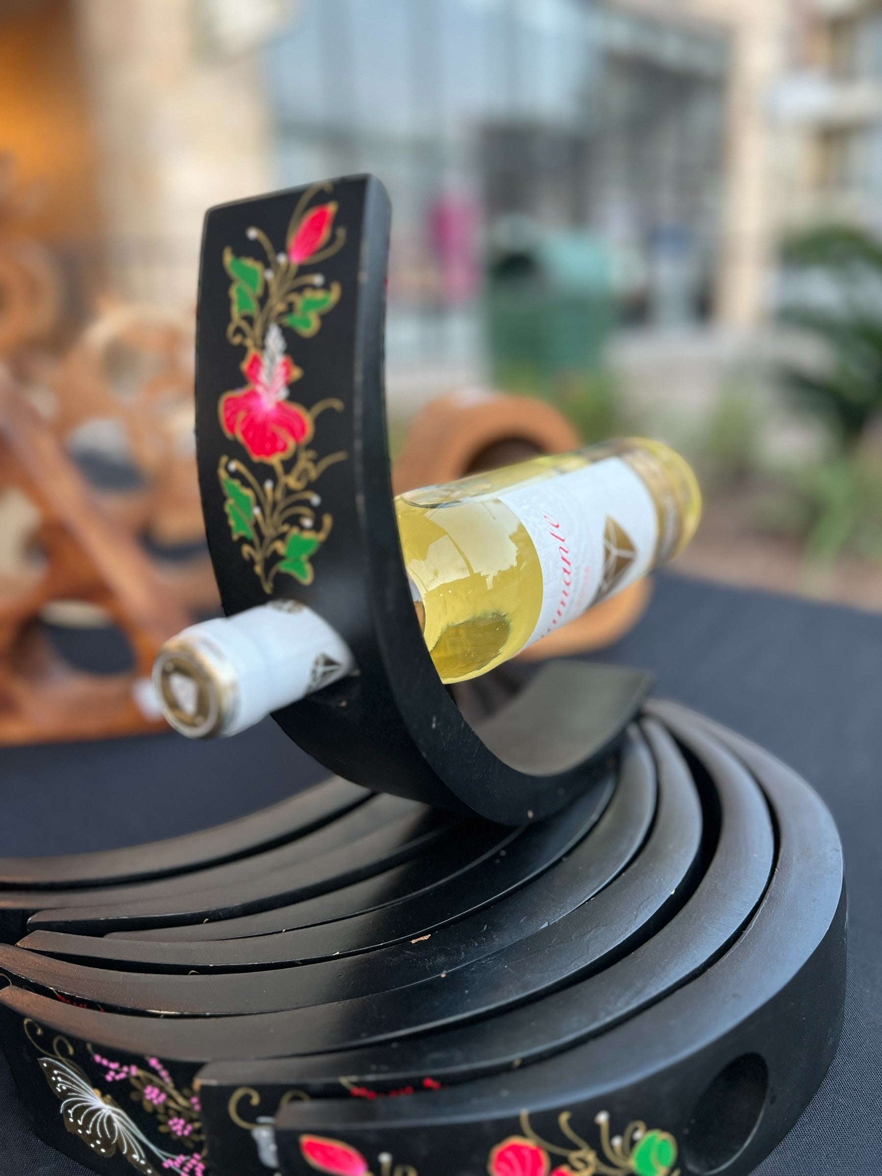 Decorative wine bottle holder with floral designs on a blurred background