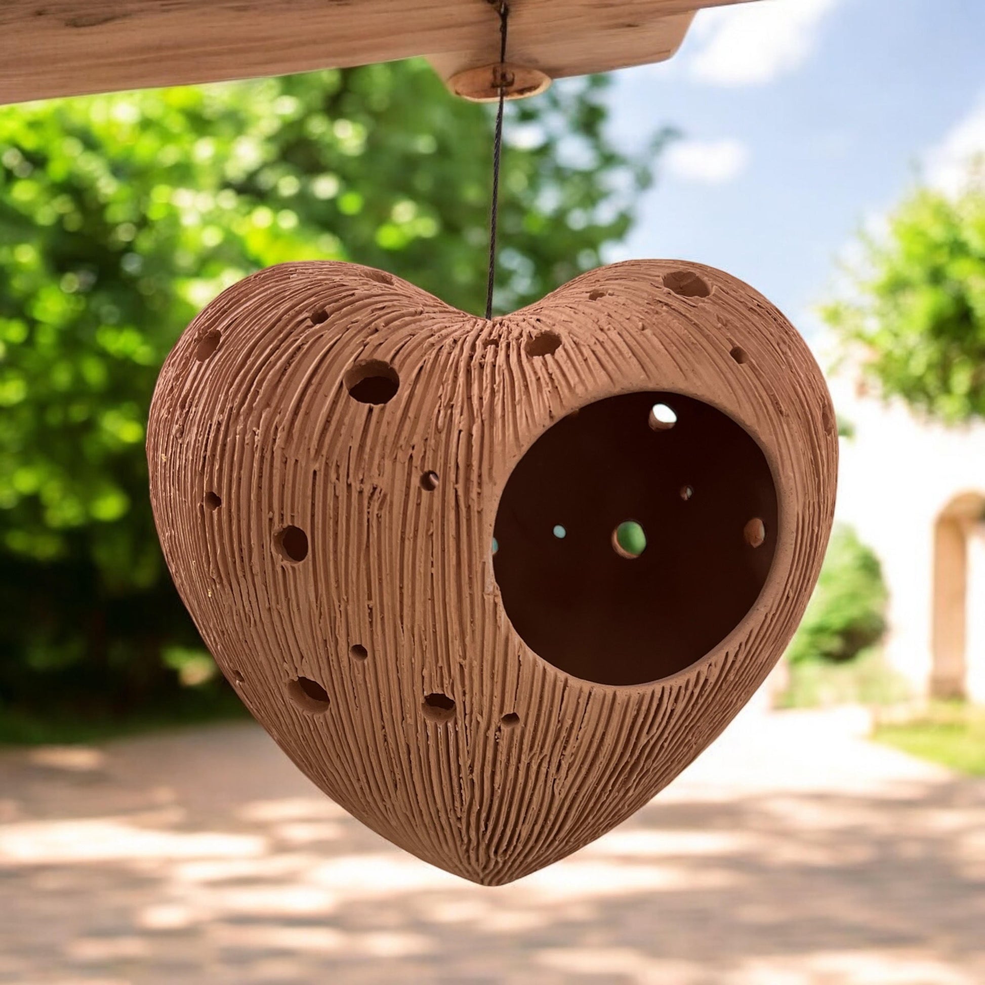 Heart-shaped Terracotta pots  hanging outdoors with greenery in the background