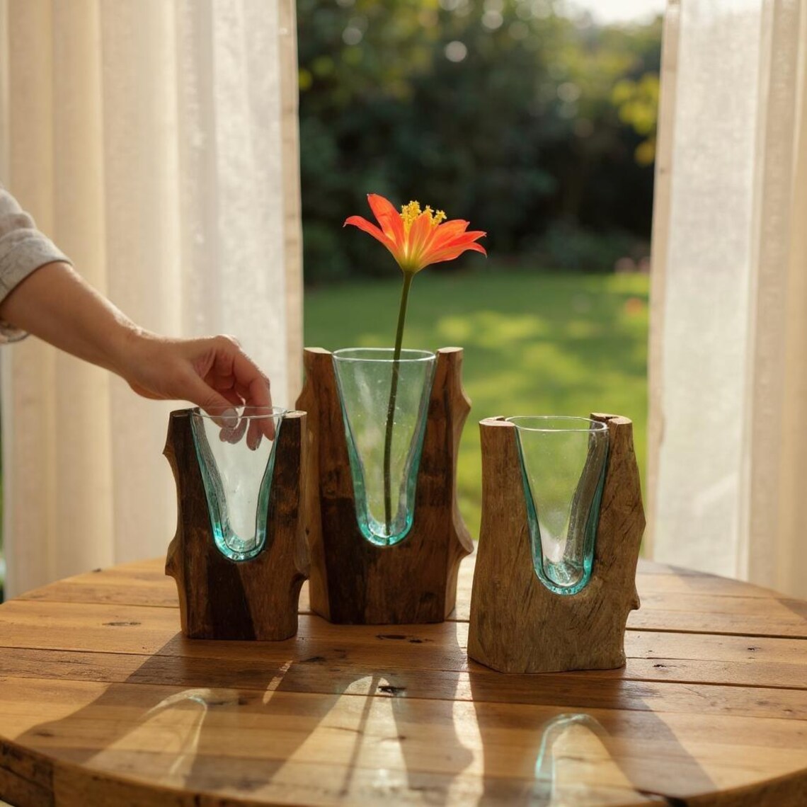 Three glass vases with wooden bases on a wooden table, with a hand reaching towards one of them.
