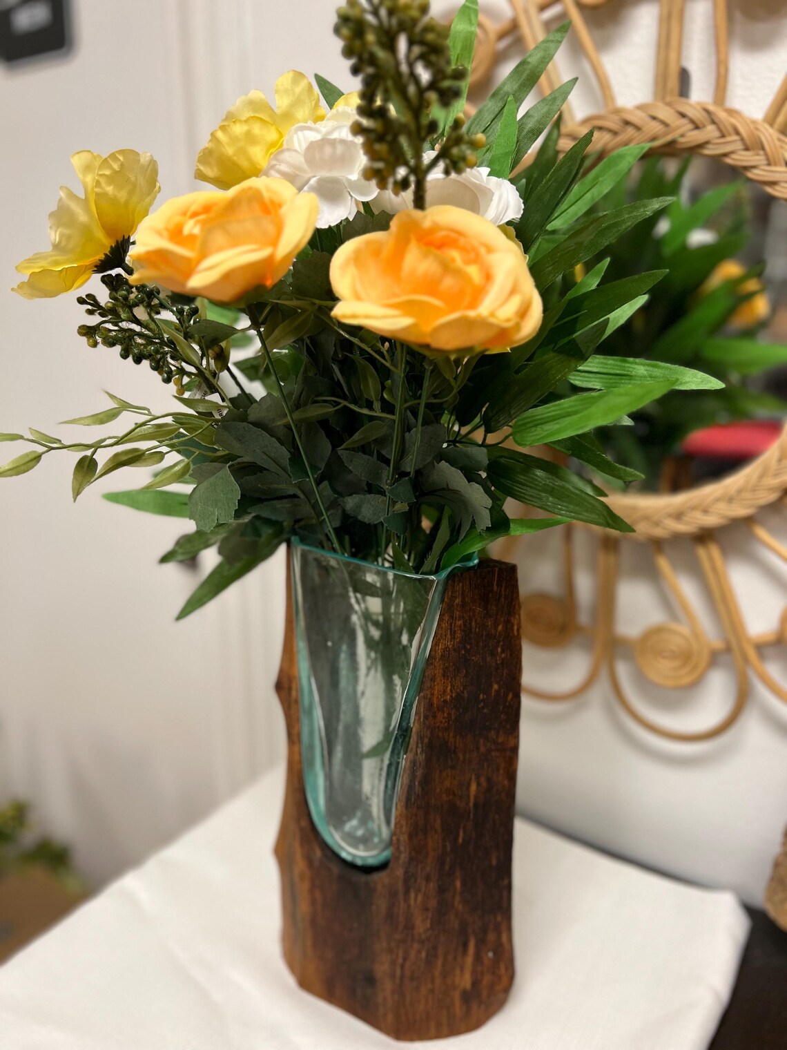 Bouquet of yellow and white flowers in a glass vase on a teakwood base.