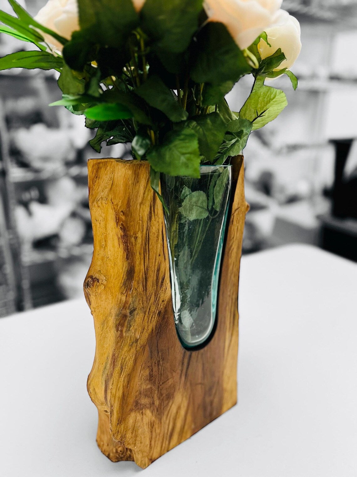 Wooden vase with a glass base holding flowers on a white surface.