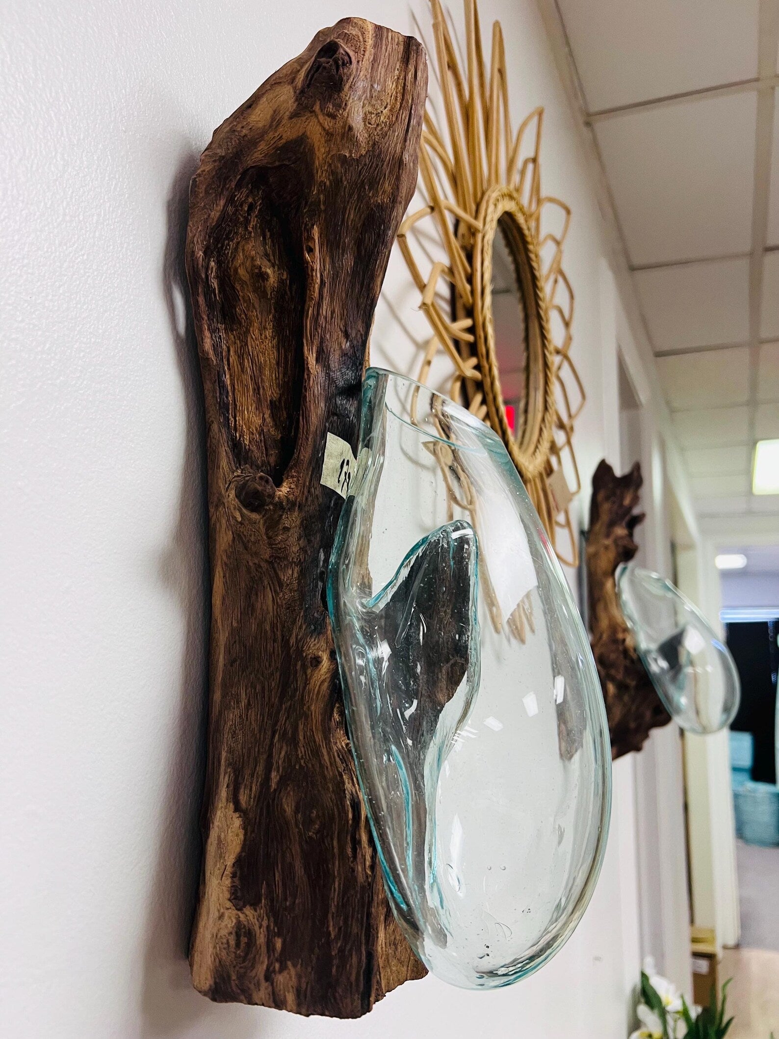 Decorative glass vase shaped like a teardrop on a wooden log against a white wall.
