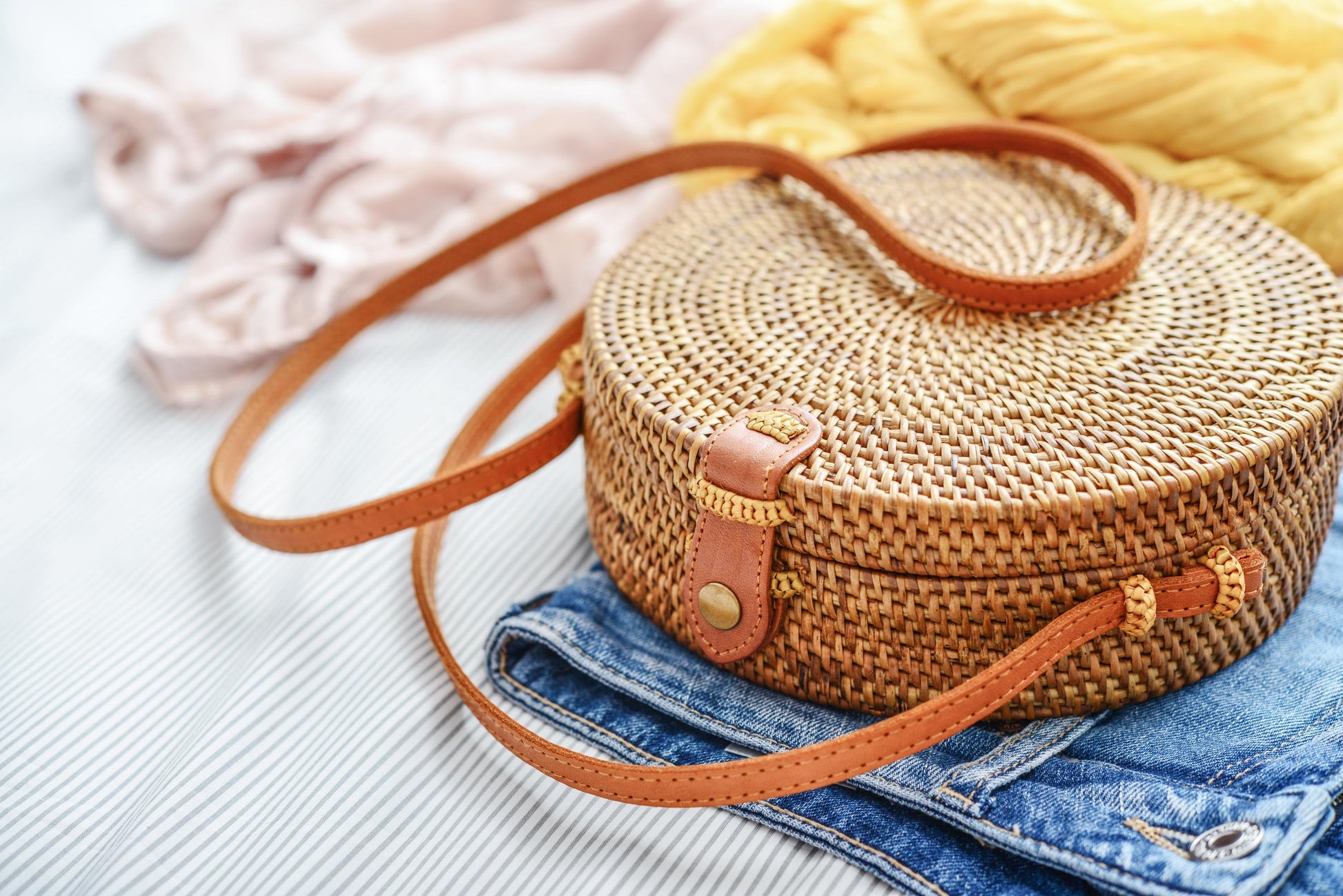 Round woven bag with brown strap on a textured surface