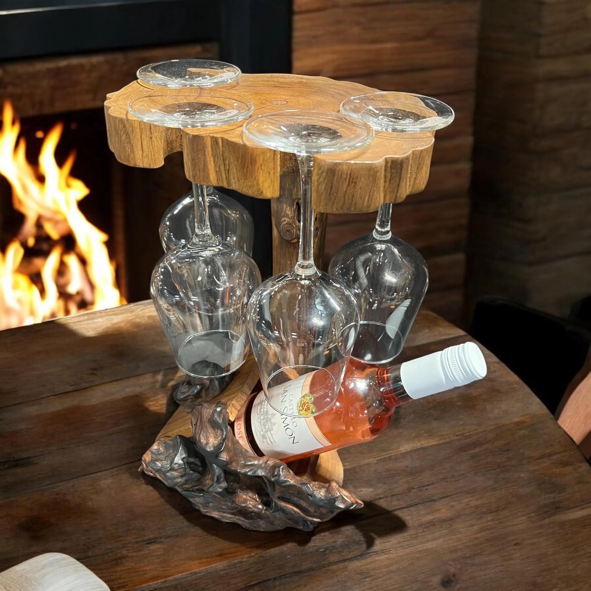 Wooden wine glass holder with glasses and a bottle on a wooden table in front of a fireplace.