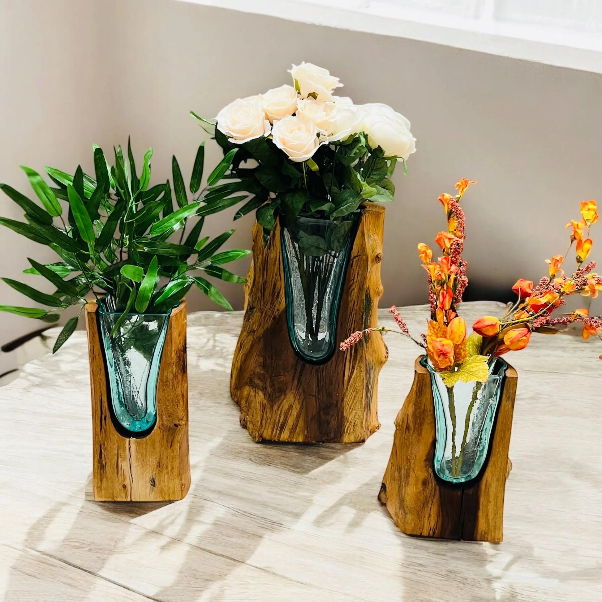 Three wooden vases with glass inserts holding plants and flowers on a table.