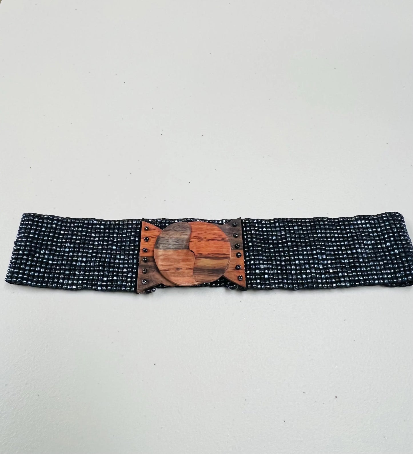 Black beaded belt with a wooden buckle on a light gray background